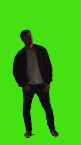 Vertical-Video-Full-Length-Shot-Of-Man-Standing-And-Waiting-Against-Green-Screen-With-Low-Key-Lighting