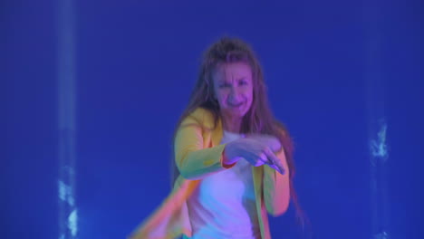 the woman dances merrily and looks at the camera in the light of strobe lights and spotlights. neon colors and crazy girl dancing to music and singing