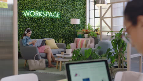 joven mujer de negocios caucásica usando computadora portátil escribiendo correo electrónico trabajando en línea compartiendo escuchando música revisando mensajes de teléfono inteligente disfrutando relajándose en una oficina moderna
