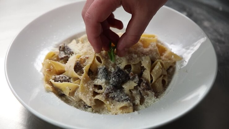 chef che prepara un piatto di pasta con salsa di crema e funghi
