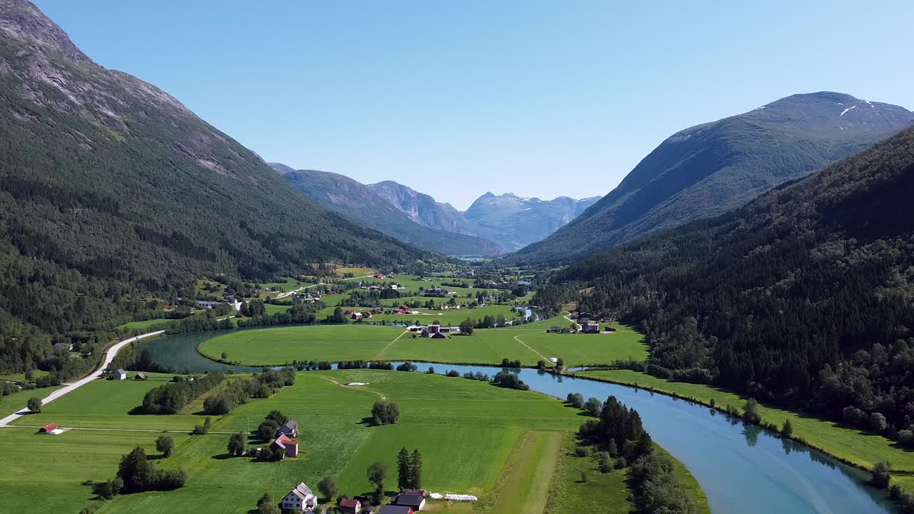 una vista aérea del exuberante valle de stryn en noruega, con campos verdes vibrantes, ríos sinuosos y majestuosas montañas bajo un cielo azul claro
