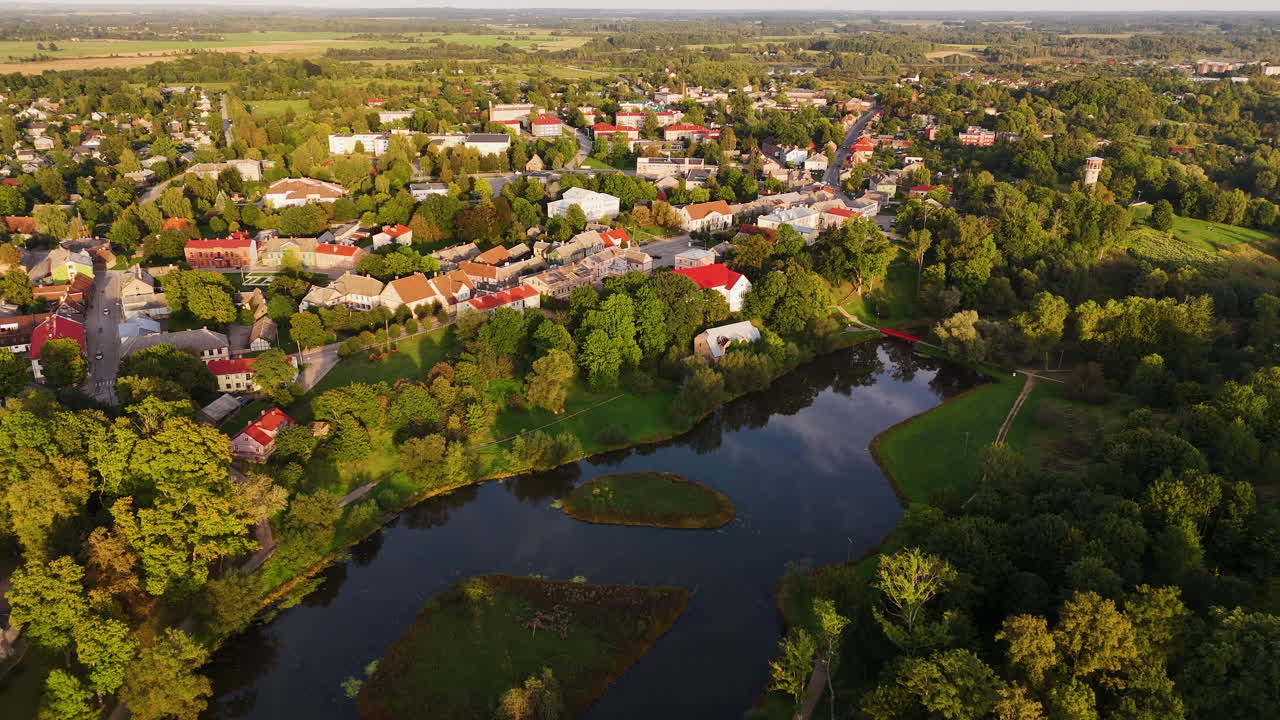 Drone footage of Aizpute, Latvia, featuring a picturesque town, lush greenery, and a tranquil lake.