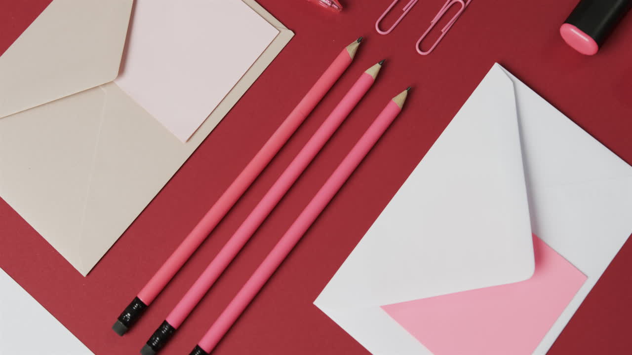vista aérea de bolígrafos, lápices y papelería dispuestos sobre un fondo rojo, en cámara lenta