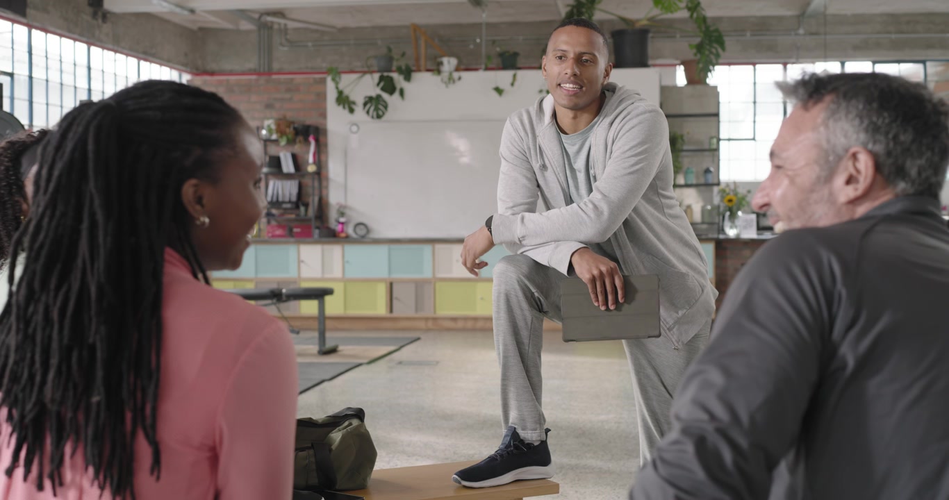 African American male coach entering, crouching on bench, using tablet, debriefing group in studio