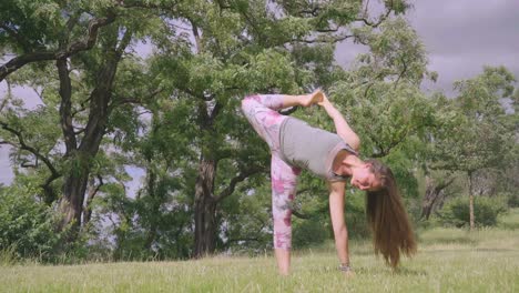 Caucasian-woman-holds-sideways-yoga-pose-in-windy-nature,-long-shot