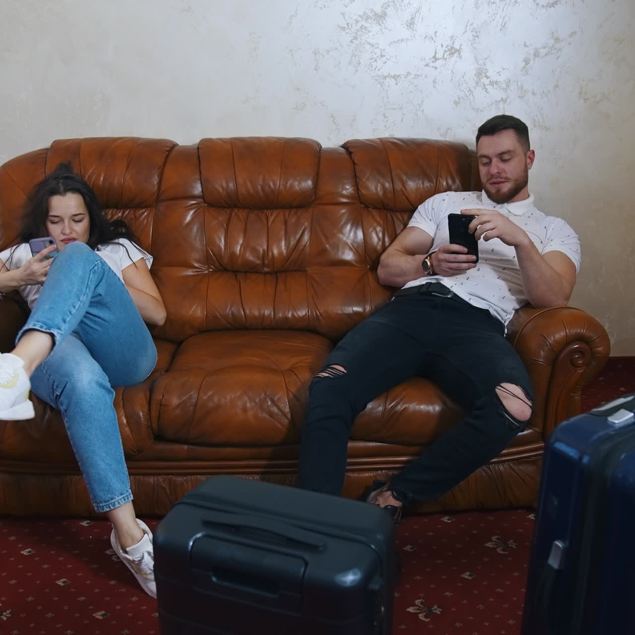 Young couple quarrel in the hotel. Beautiful woman and handsome man sitting on a couch near suitcases before leaving the hotel. The end of family vacation