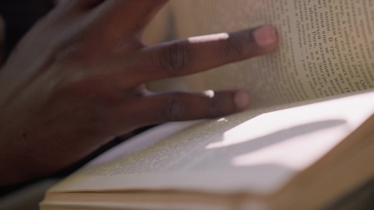Close up of person hands turning pages of open book with text visible. focus remains on hand movement and page interaction capturing texture details like skin lines or paper edges. Soft