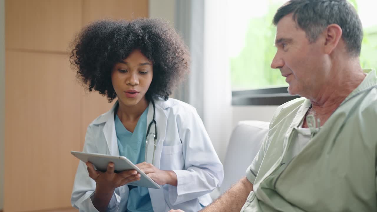 African American female medical doctor using digital tablet explain the symptoms to the patient after treatment or talking with old man patient in the hospital.