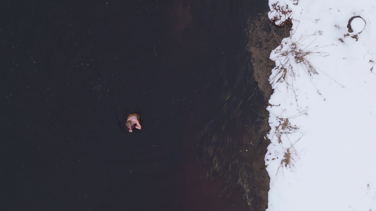 An ice bathing woman finishes her daily winter swim, aerial top down
