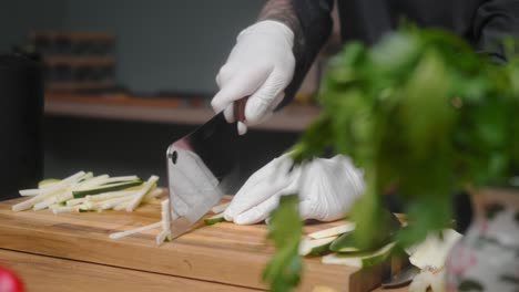 fresh zucchini being sliced on a wooden board by young professional male chef in an elegant black shirt with tattoos