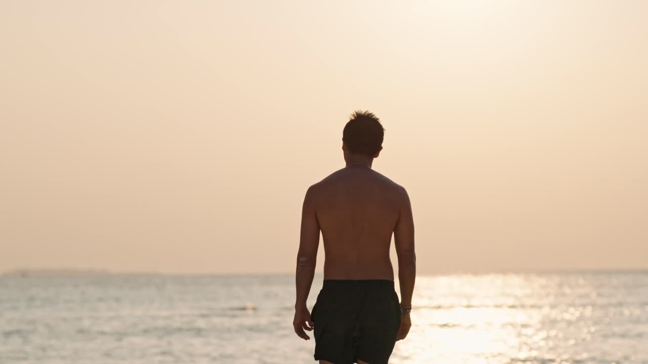A solitary man stands on a pristine beach in the Maldives, gazing at the vibrant sunset over the calm ocean.