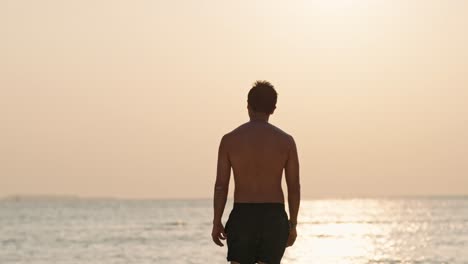 a solitary man stands on a pristine beach in the maldives, gazing at the vibrant sunset over the calm ocean.