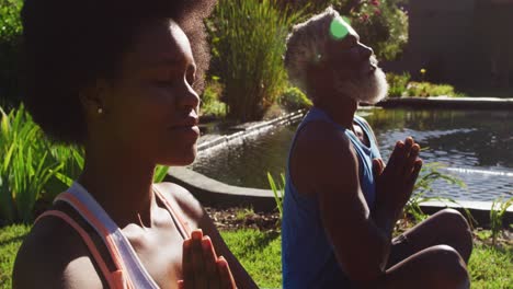una pareja de ancianos afroamericanos haciendo ejercicio practicando yoga sentados meditando junto al estanque en un jardín soleado