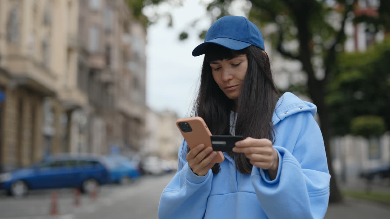 Woman holding credit card and mobile phone outdoors in city