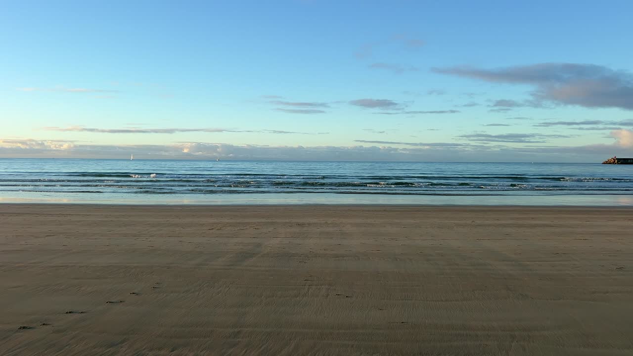Wide view of a serene empty beach at sunset, calm waves