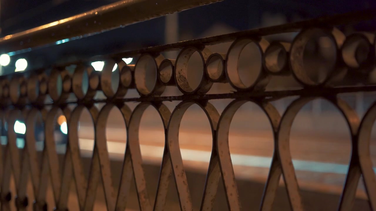 Köprü korkuluklarının arkasında yumuşak ve bulanık bir bokeh efekti yaratan renkli araba ışıklarıyla gece trafiği sahnesi; atmosferik şehir hareketini, yol trafiğini ve canlı şehir ışıklarını yakalıyor