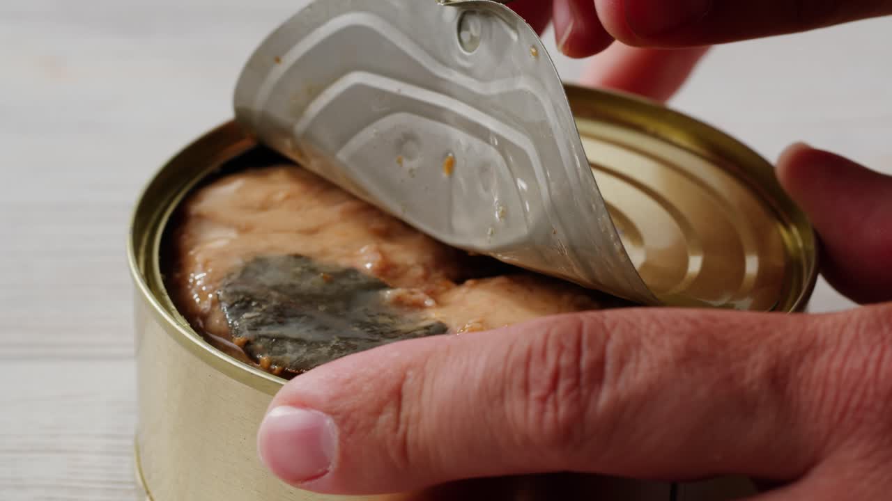 Smoked cod liver in oil in open tin can with fresh greens on wooden table. Seafoods delicacy. High quality 4k footage