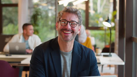 Portrait-Of-Mature-Businessman-Wearing-Glasses-Working-On-Laptop-At-Desk-In-Office