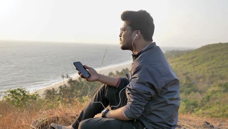 young traveler or tourist wearing jacket and eyeglasses siting on a mountain top