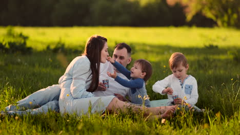 Vater,-Mutter-Und-Zwei-Kinder-Sitzen-Bei-Sonnenuntergang-Auf-Einer-Wiese-Und-Essen-Im-Sommer-Ein-Eis-Bei-Einem-Picknick.