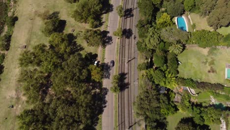 Toma-Aérea-De-Arriba-Hacia-Abajo-De-La-Conducción-De-Automóviles-En-La-Calle-Al-Lado-Del-Ferrocarril-Durante-La-Luz-Del-Sol-En-La-Ciudad-De-Buenos-Aires