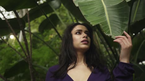 indian woman touching giant leaf in jungle with a sun behind slowmotion