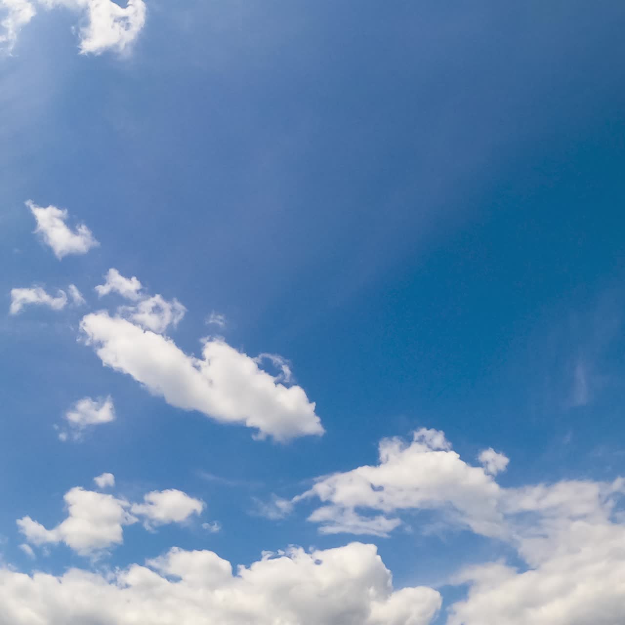 Beautiful blue summer sky with white clouds moving slowly. Soft fluffy cloudscape changing shape from low angle view