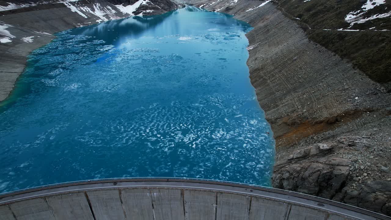 4k Drone Aerial Shot Of Vibrant Blue Glacial Water Of Lac de Moiry Dam Surrounded By Massive Snow Covered Mountain Peaks Reflecting On lake In Grimentz Switzerland