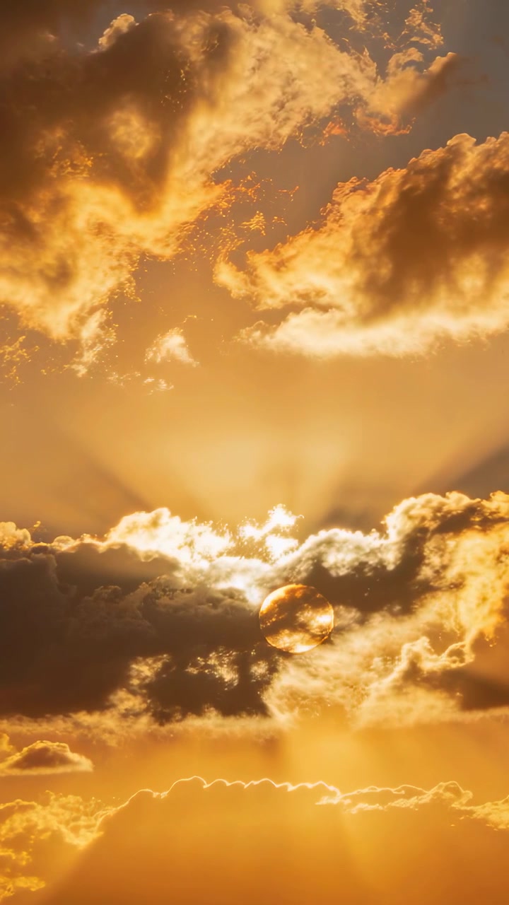 Vertikales Video: Zeigt teilweise verdeckten Sonnenaufgang am offenen Himmel, mit ziehenden Wolken, die Strahlen werfen.