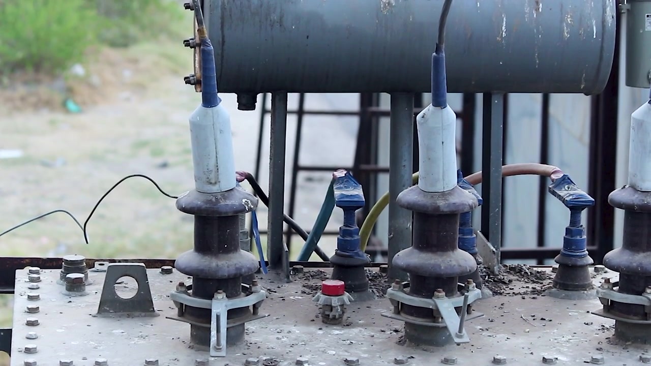 Weathered electric transformer with ceramic insulators and corroded fittings in rural India. Essential broll for power grid failure, energy access, and infrastructure docs.