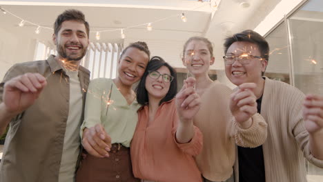 a multiethnic group of friends looking at the camera, smiling and shaking some sparklers 2