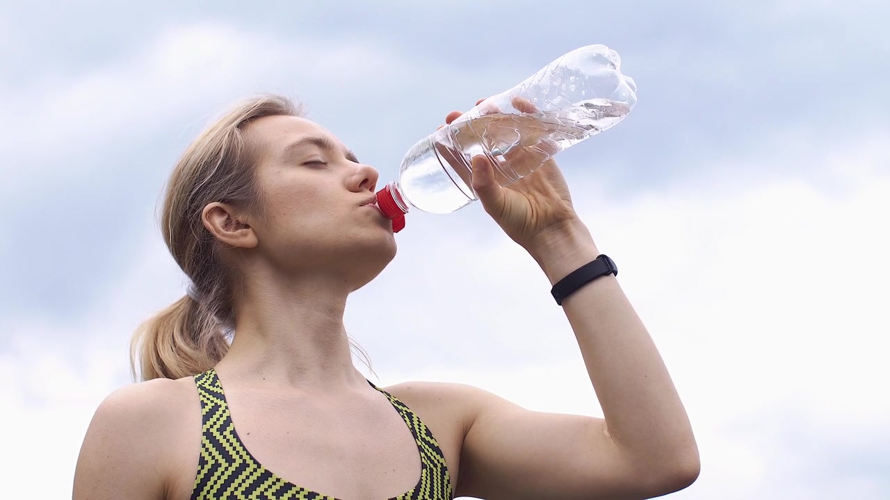 Giovane donna che beve acqua da una bottiglia all'aperto