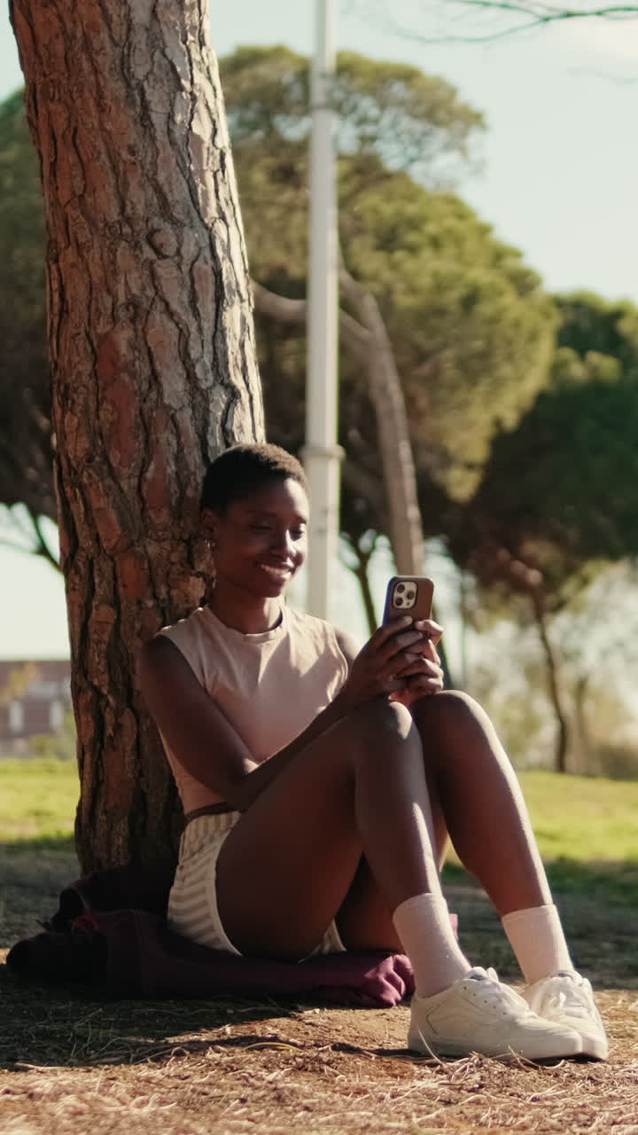 Giovane donna che si rilassa al parco, usa lo smartphone e sorride