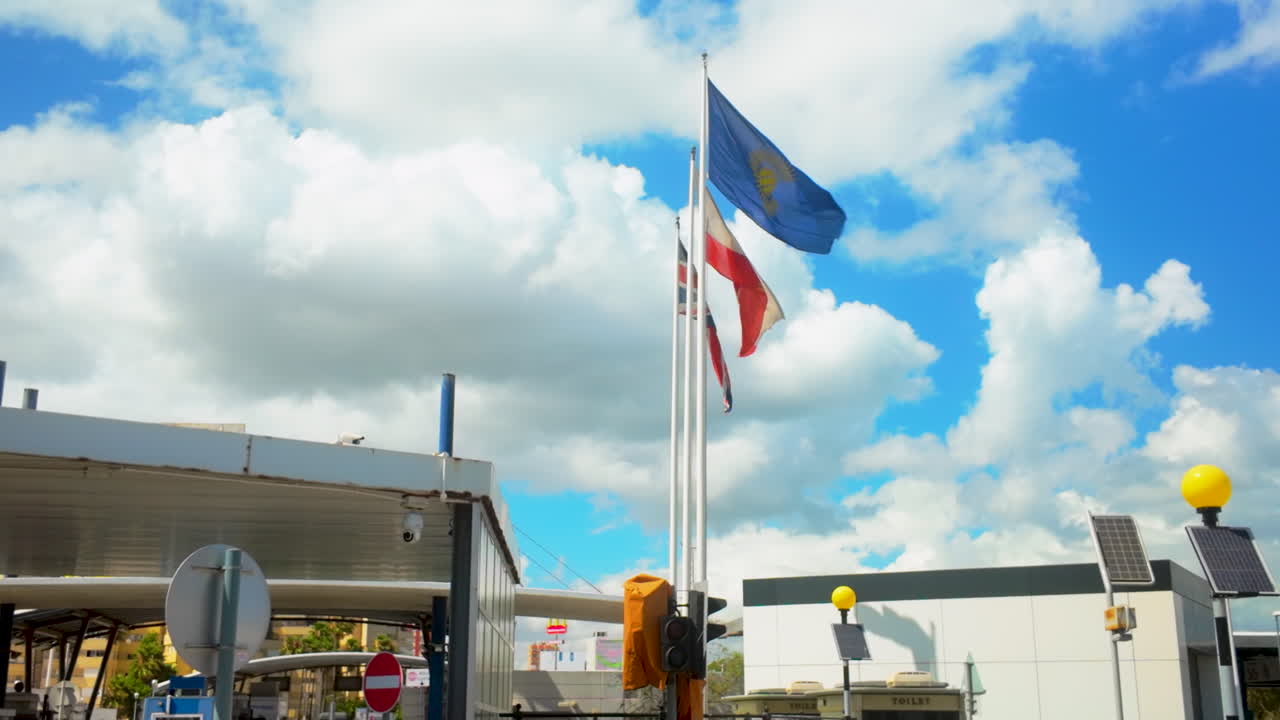 Flags of Gibraltar, the United Kingdom, and the European Union waving in the wind against a bright blue sky