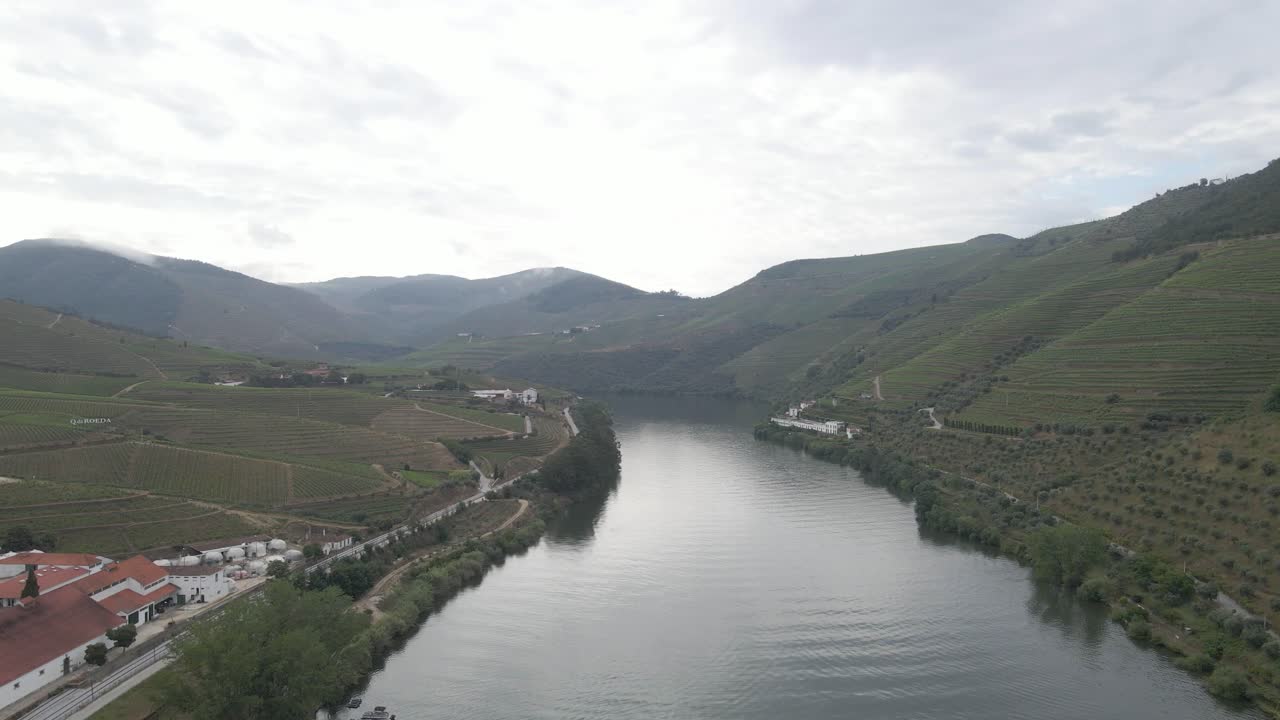 Vista aerea della città vinicola di Pinhão, Portogallo, drone che avanza sul fiume Douro mostrando le piantagioni di viti e le montagne sullo sfondo.