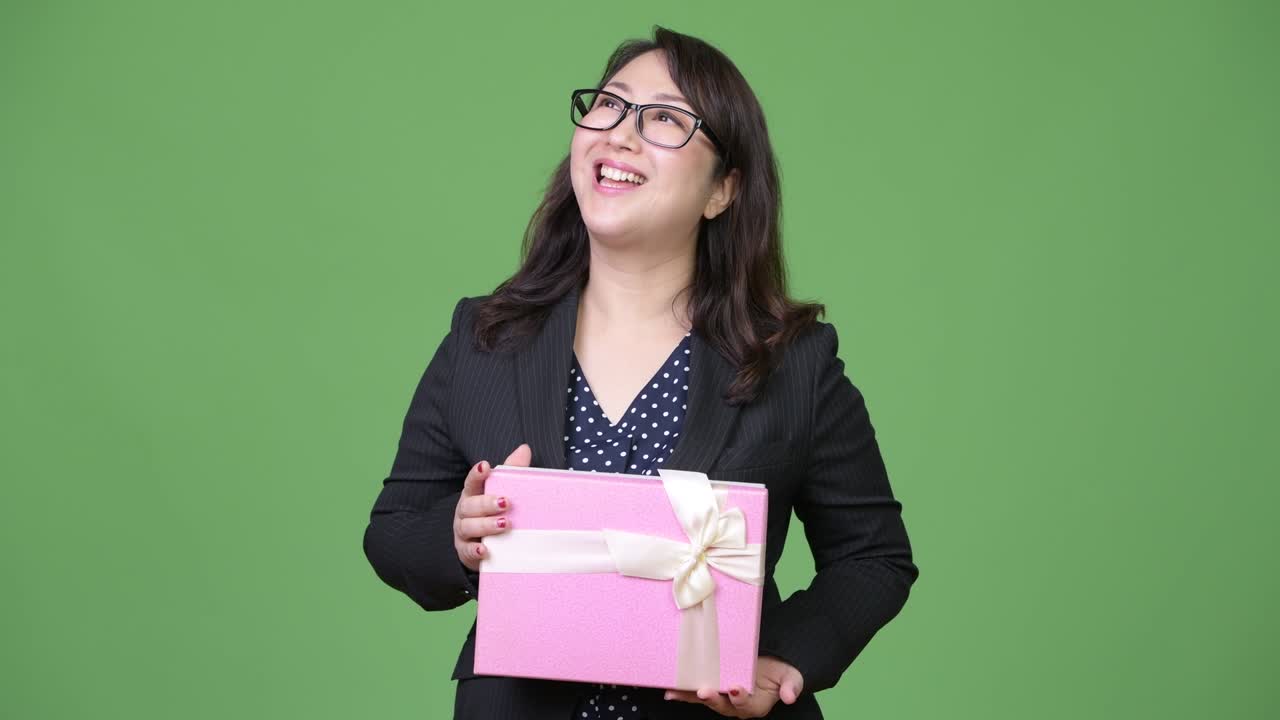 Mature beautiful Asian businesswoman thinking while holding gift box