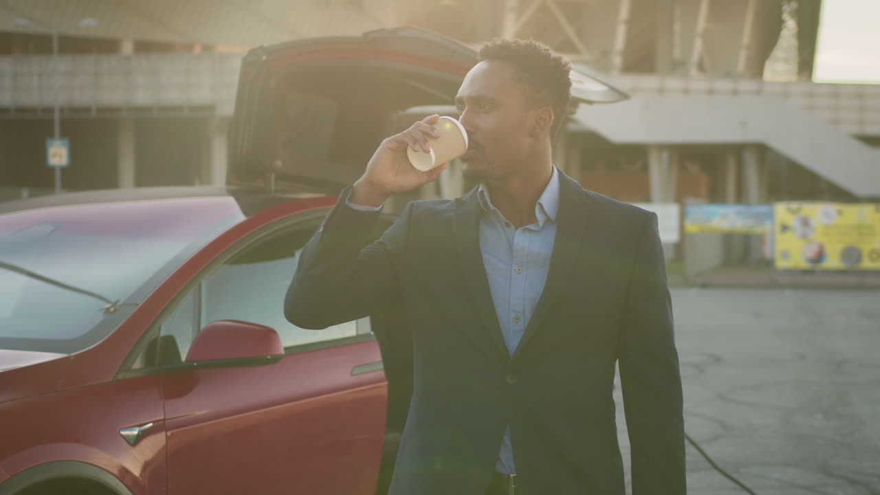 Uomo d'affari che beve caffè vicino a un'auto elettrica