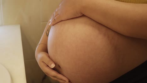 pregnant young female holding her baby belly in the bathroom