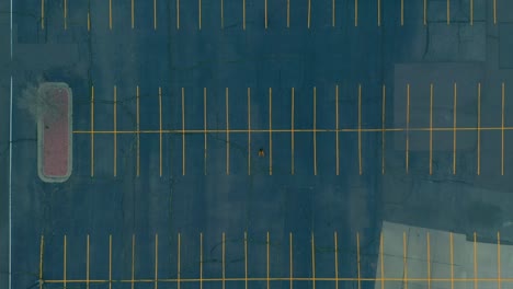 Top-down-aerial-shot-of-biker-riding-through-a-large-empty-parking-lot-during-stay-at-home-orders