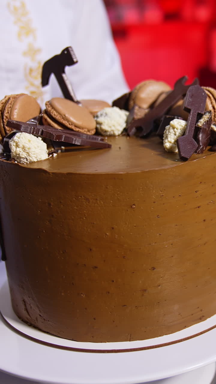Pastry cook rotates beautiful chocolate cake on the stand. Ready-made dessert product manufactured at the confectionary. Close up. Vertical video