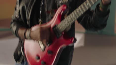 A-guitarist-close-up-during-the-performance,-The-electric-guitar-color-is-red-and-the-guitarist-wore-a-black-rock-star-jacket,-other-band-is-in-the-background