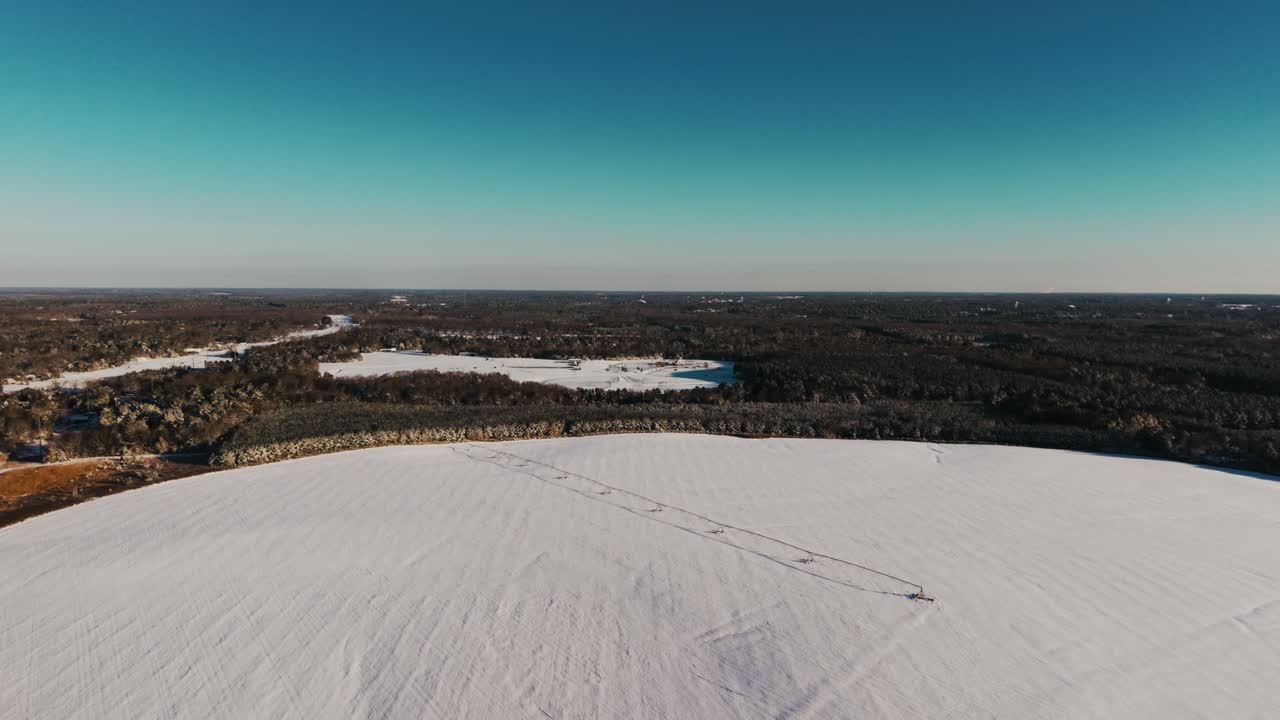 An aerial drone view showcasing a snow-covered pivot irrigation system in a vast field with a treeline backdrop, captured in South Georgia's rare snowfall.