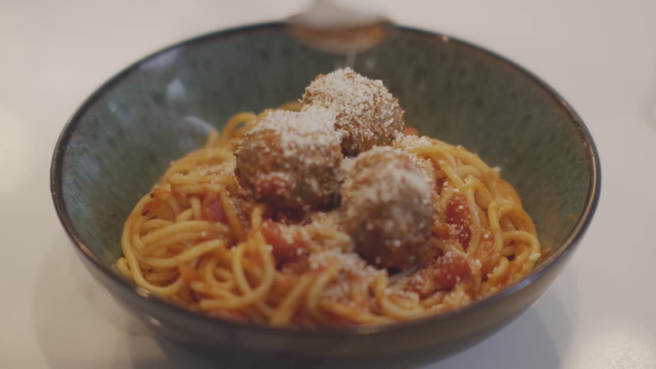 Un primo piano al rallentatore di parmigiano grattugiato su un piatto caldo di spaghetti con polpette