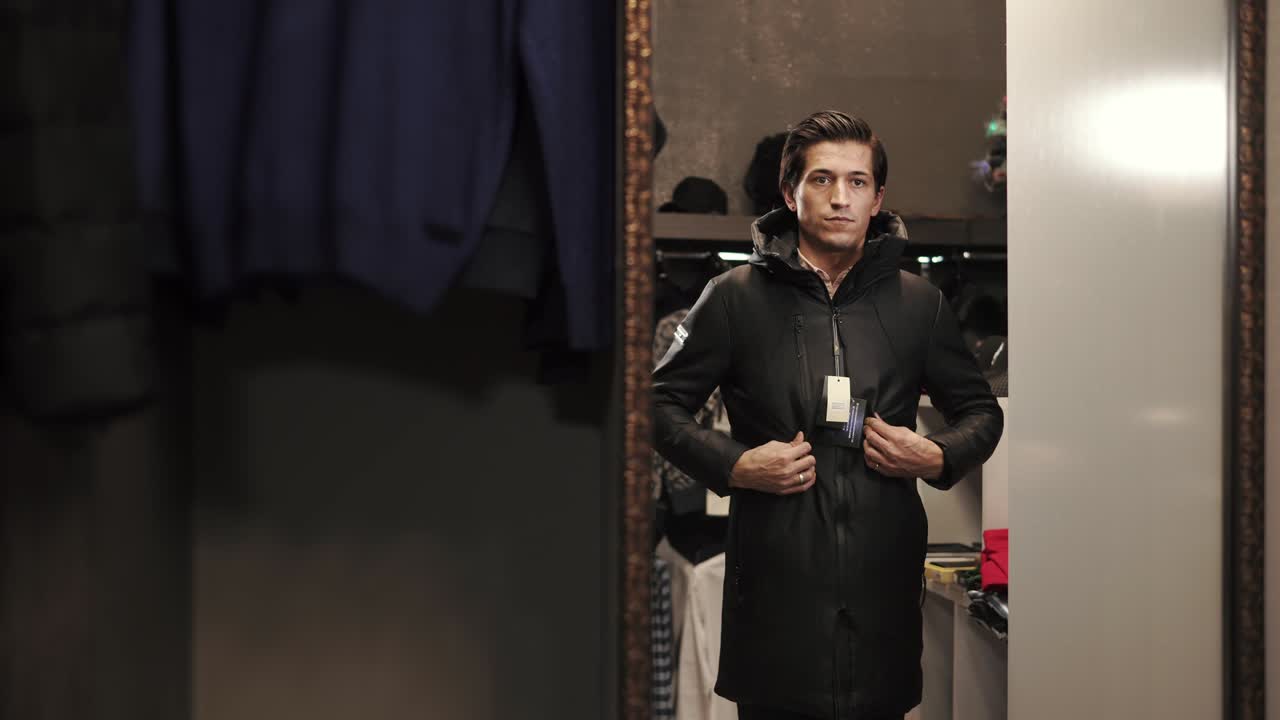 A young man buttoning his jacket and looking in the mirror at a clothing store
