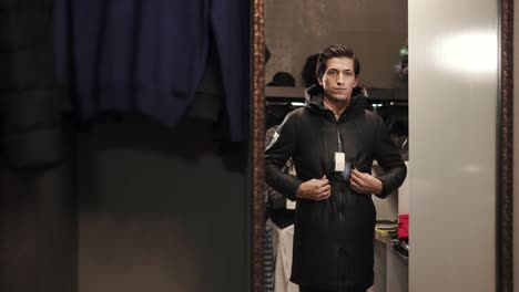 a young man buttoning his jacket and looking in the mirror at a clothing store