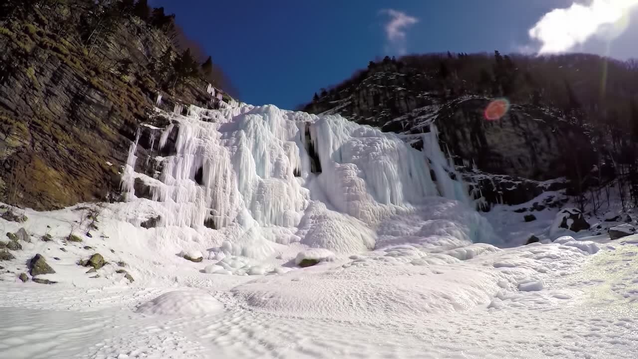 Spectacular frozen waterfall showcases stunning icy formations surrounded by rugged cliffs under a clear blue sky. A perfect winter wonderland scene inviting exploration.