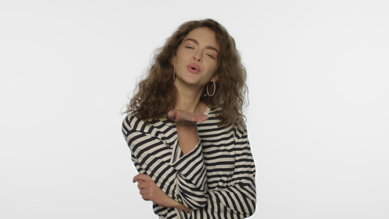 joven mujer envía un beso de aire en el estudio blanco