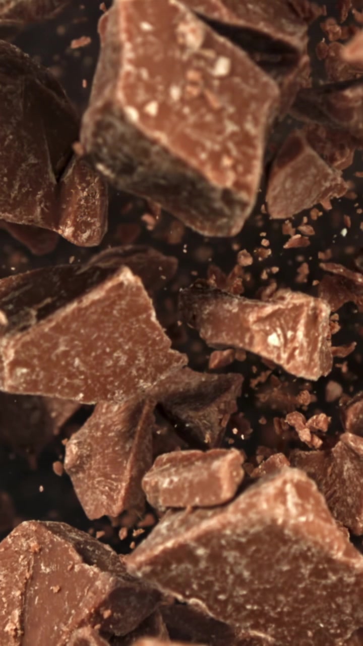 Pezzi di cioccolato che cadono al rallentatore con particelle di cacao
