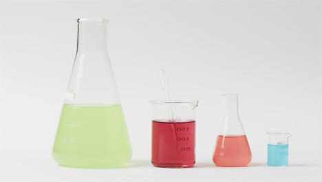 Coloured-liquids-in-flasks-on-white-background-with-copy-space,-slow-motion