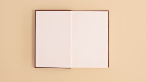 brown leather hardcover vintage book appear and open with copy space on beige background. stop motion flat lay